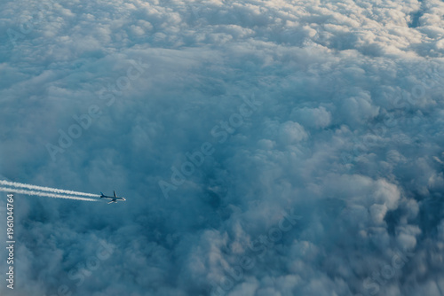 Foto Aerial view of an airplane flying above sea of clouds with long condensation trails
