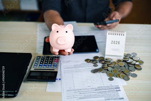 Foto Hand holding piggy bank above financial documents with coins, calculator, and calendar on desk, symbolizing saving money, tax planning, and personal finance management