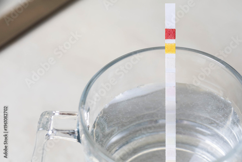 Water test strip immersion in clear glass of water displaying chemical reaction color changes measurement of water parameters for quality analysis of drinking water for safety and health purposes