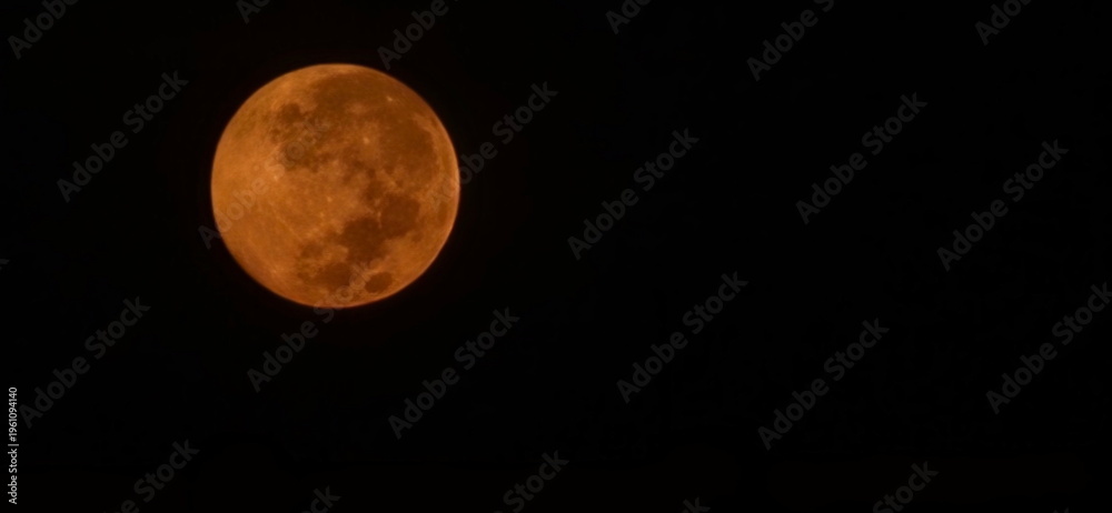 Obraz premium Supermoon in center of image. Luminous orange moon with ethereal glow against pitch black sky. Photograph of an full moon in a dark sky. Image taken with a mobile phone lens with maximum zoom. 