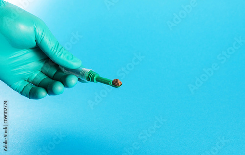 Fotografía A laboratory technician's hand in a green glove holding a stool sample tube against a blue background