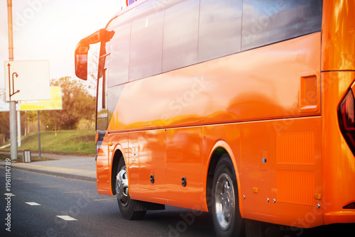 Orange passenger bus movement on urban road at sunset with bright sun flare