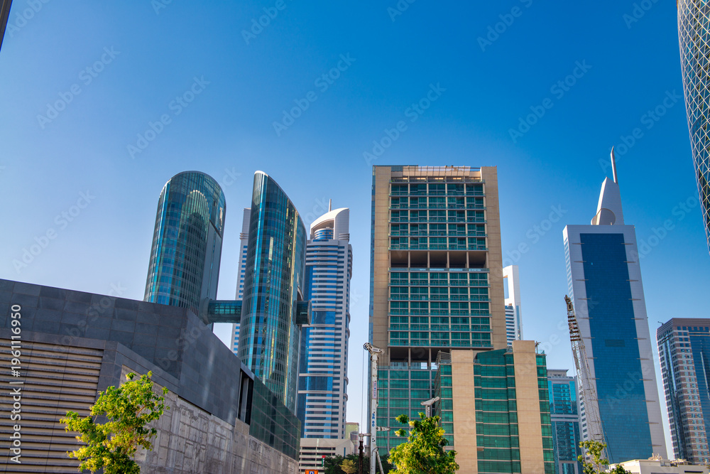 Obraz premium Downtown Dubai's gleaming skyscrapers under intense desert sunlight with modern towers reflecting blue skies and golden rays