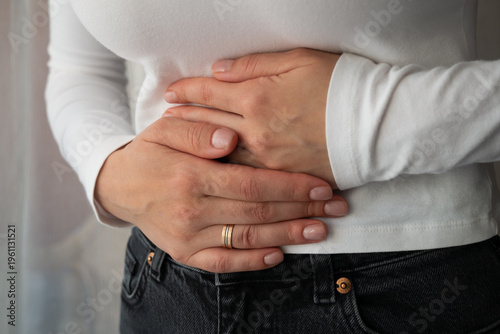 Woman with stomach pain, clutching upper abdomen, suffering from bloating or digestive problems, healthcare and wellness concept.