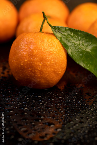 wet orange small tangerines with green leaves are reflected on a black mirror , a group of ripe sweet tangerines with green leaves covered with drops of clear water with reflection on a black glass
