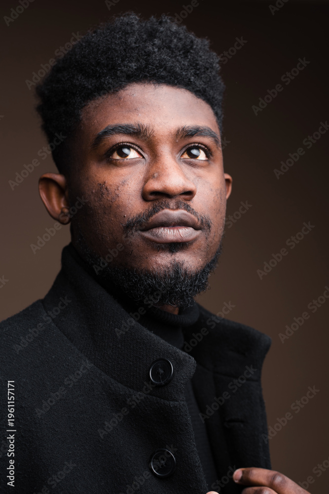 Obraz premium Young Black man with textured hair and beard looking upwards thoughtfully