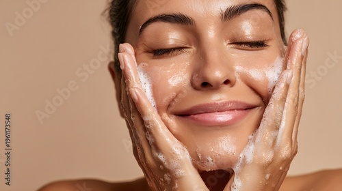 Closeup of a woman washing her face with a foamy cleanser, eyes closed in a calm expression. Soft lighting, warm tones, freshness and gentle skincare