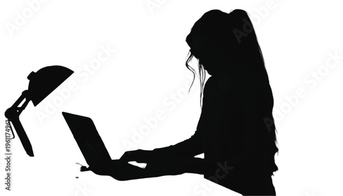 Woman silhouette sits working on a portable computer next to an illuminated desk lamp.