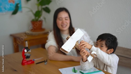 Happy asian mother and son having playful time with wood airplane at home - Nanny, daycare, education and childhood concept - Focus on boy hands and toy