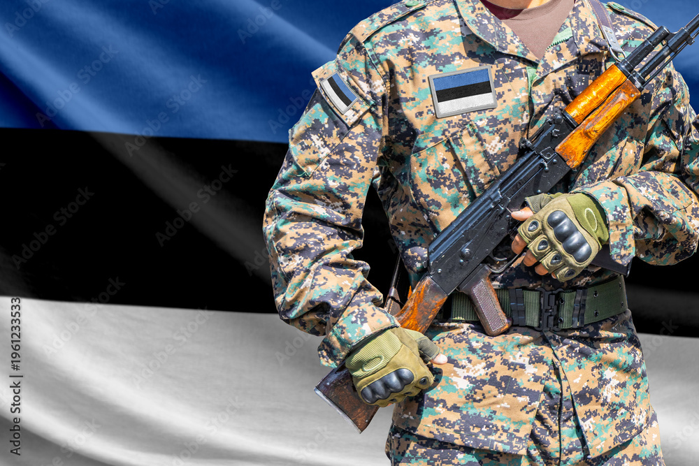 Fototapeta premium Estonia flag with soldier in military uniform holding assault rifle in front of it