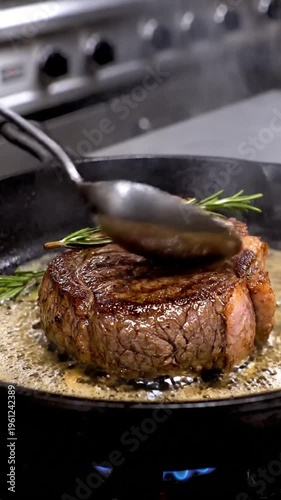Grilled steak cooking in a sizzling hot pan with rosemary and steam, on a stovetop in a kitchen, possibly for a restaurant or recipe