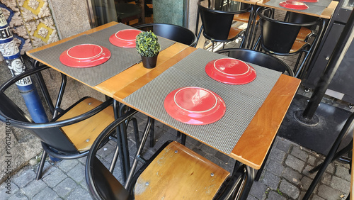 Outdoor cafe table with red plates and chairs on city street. Simple restaurant setup with tableware and seating. Urban dining scene suitable for hospitality, food service and lifestyle themes.