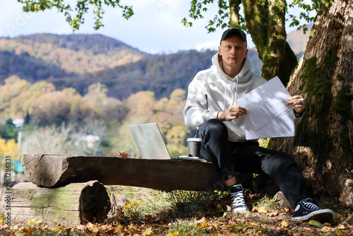 Canvastavla Man holding forth blank papers near laptop setup in vibrant autumn outdoor works