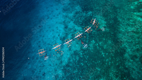 Aerial view of traditional outrigger boats slicing through the turquoise waters off the coast, a vibrant tapestry of blues and greens blending seamlessly, Oslob, Cebu, Philippines.