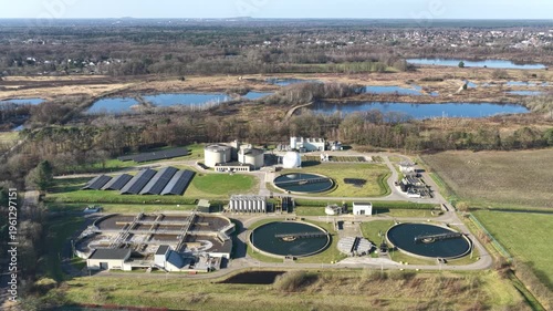 Diepenbeek, Belgium. Aerial drone footage of wastewater treatment facility with circular basins and solar panels in rural landscape