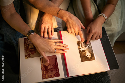 Bilde på lerret Close up of women hands pointing at family photo album, reviewing printed memories and sharing personal history