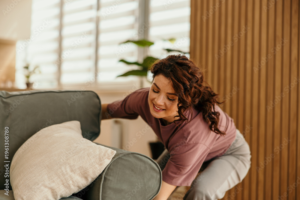 Obraz premium Young woman adjusting cushions on a sofa at home