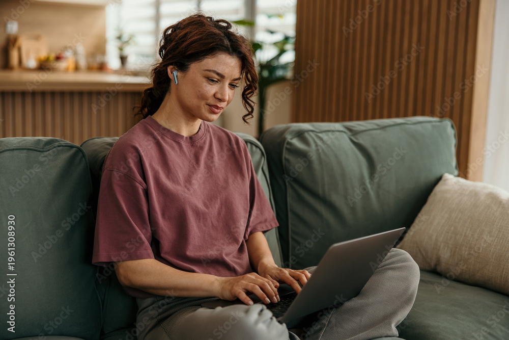 Obraz premium Woman working remotely from home using laptop and earbuds
