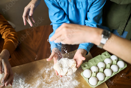 Overhead shot of family hands preparing dough and sprinkling flour beside eggs during home baking. Supporting cooking class, family bonding, recipe content, food marketing use