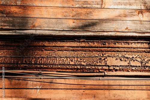 The image features a composition of horizontal lines and diverse materials, dominated by warm ochre and rust tones. From sun-bleached wooden planks at the top to heavily corroded metal and modern cabl