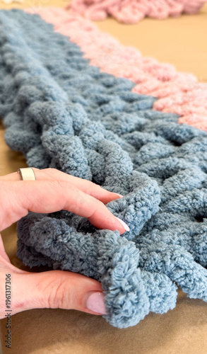 Photos Hand holding chunky knit blanket on craft workspace surface