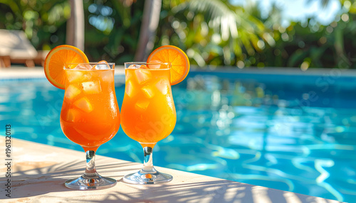 Aperol Spritz cocktails poolside. Two refreshing orange drinks in stemmed glasses on a pool edge, with palm trees, blue water, and shadows on a sunny day.