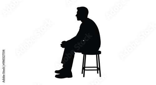 A man sits on a stool facing left in stark contrast silhouette