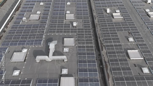 Genk, Belgium. Aerial drone glide over industrial rooftop covered with solar panels showcasing renewable energy infrastructure. Forward drone flight.