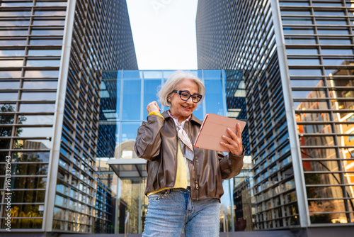 Фотография Senior woman celebrating success using a tablet in a business district