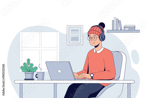 Young woman works on a laptop while wearing headphones and a knit hat