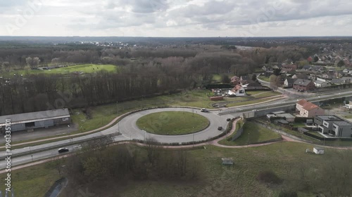 Genk, Belgium. Smooth lateral drone movement over suburban roundabout with surrounding residential landscape. Orbital drone flight.