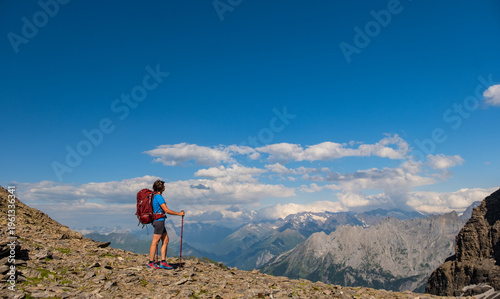 A lone hiker pauses on a rocky peak, gazing at the breathtaking mountainous terrain below. Sporty woman hiking in Switzerland alps. Heathy lifestyle, sport, beauty in nature. Grindelwald valley, Swizz