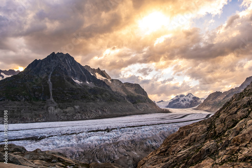 Aletsch Glacier stretches through the Swiss Alps, surrounded by rugged mountains and a colorful sky at sunrise. The glacier flows down between the peaks, showcasing natural beauty.