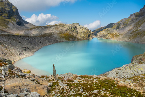 Captivating landscape of Pizol Wildsee lake in the Swiss Alps, featuring tranquil turquoise water amid rugged peaks enveloped by mist and clouds, creating a dramatic mountain scene