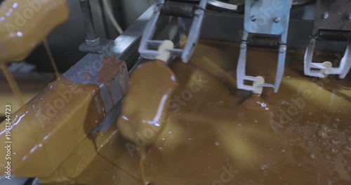 Chocolate-coated popsicles being produced at an ice cream factory. A close-up of the popsicle production line. Ice cream is dipped into melted chocolate close-up. Chocolate dripping from ice cream. 