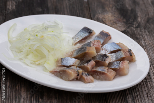 Salted herring with onions on a white plate, the perfect appetizer for vodka.