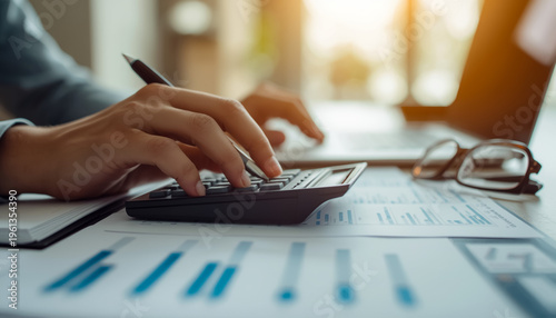Close-up of hands using calculator with pen on financial documents and glasses on desk