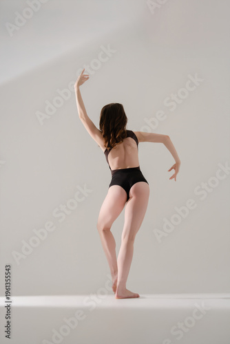 Graceful dancer in black leotard performing contemporary movement, rear view.