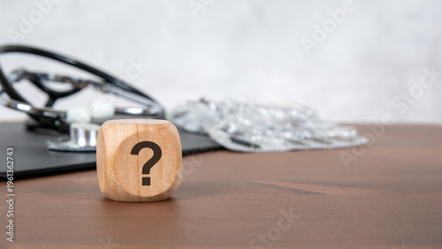 Question mark on wooden block with blurred stethoscope and pills. Medical advice, health diagnostics and healthcare consultation concept.