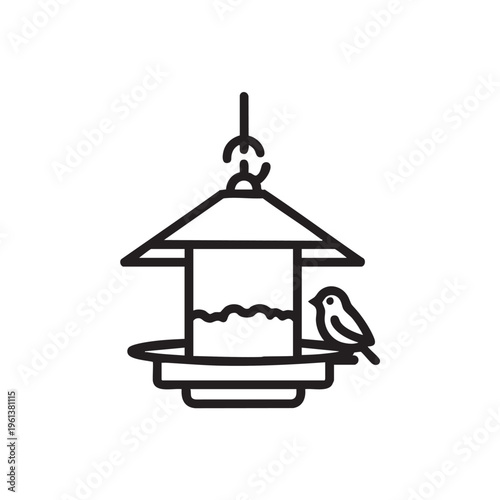 A bird perches on a hanging bird feeder with a roof and tray outdoors.