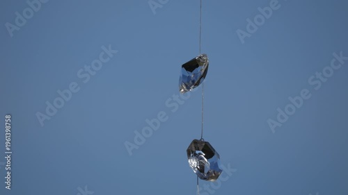 4K telephoto-style shot of decorative glass crystals suspended on a string, gently swaying in the wind against a clean blue sky background. The composition emphasises minimalism, negative space, and s