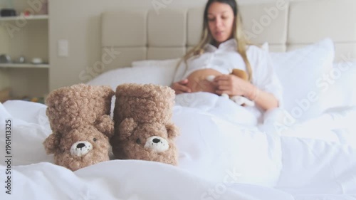 Expectant mother holding headphones on her belly while resting in bed