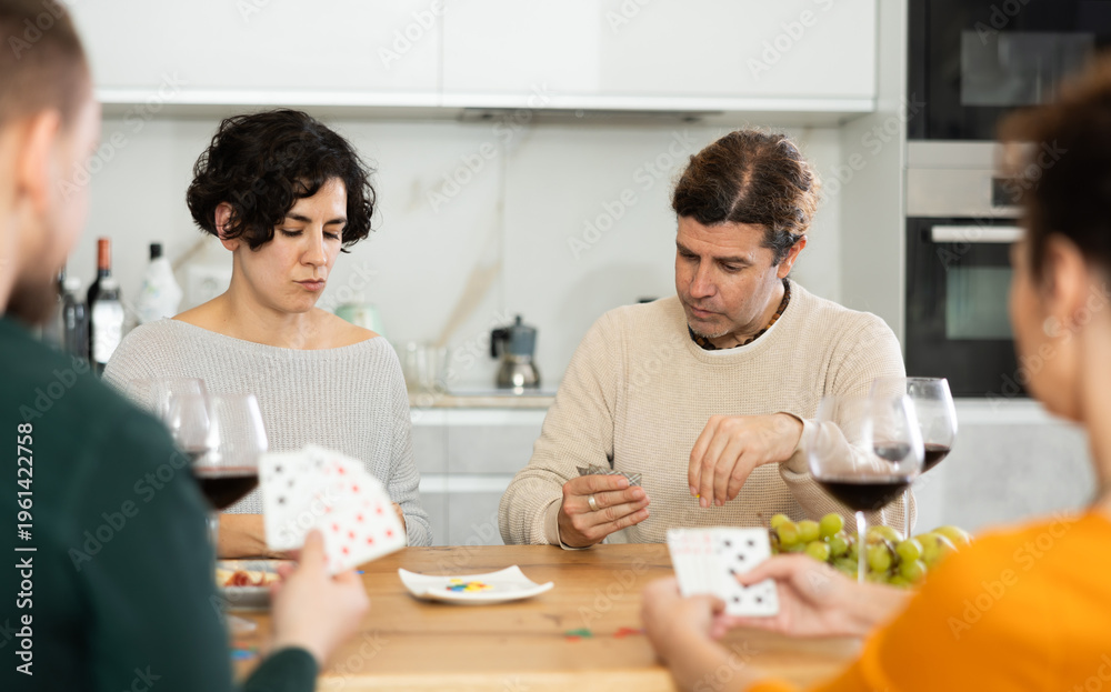 Fototapeta premium Happy group of friends playing poker cards and drinking wine at home