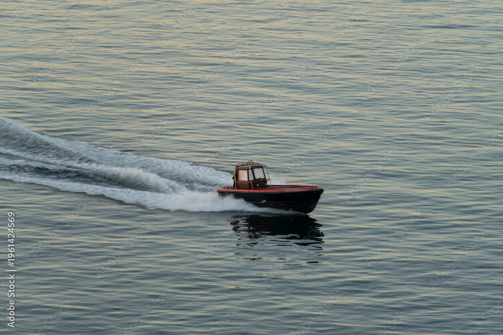 Fototapeta premium Small motorboat speeding across calm sea with wake