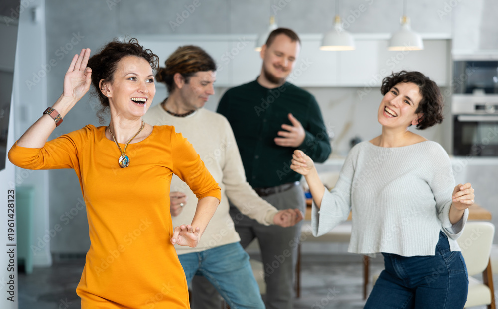 Fototapeta premium Four adult friends dancing and singing at home. Cheerful women and men enjoy music together. Happy party people celebrating friendship