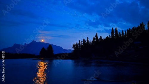 Moonlight reflects on Jack Lake with mountains and trees in the background near Banff, Alberta, Canada