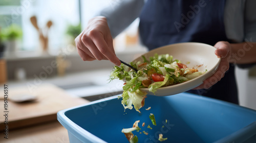 Throwing away leftover salad into kitchen bin, food waste, home cleanup, eco concept, realistic close-up image close crop of a person in an apron emptying leftover food from a shal