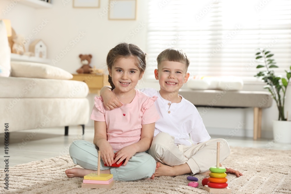 Fototapeta premium Smiling little friends with toy pyramids sitting on floor at home
