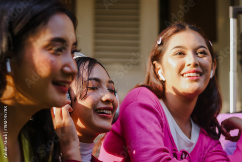 Three beautiful young women radiate joy, sharing smiles and sunlight while enjoying music. They showcase youthful exuberance and connection, highlighting vibrant friendship during a peaceful day.
