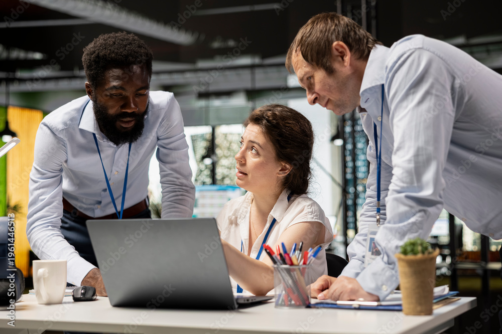 Obraz premium Diverse corporate employees in office workspace review financial data and investment reports on laptops. Professional woman conducts project briefing with male colleagues, analyzing company statistics